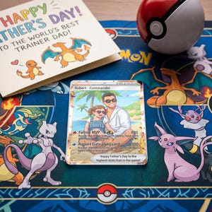 Pode incluir: Um cart&atilde;o de Dia dos Pais com o texto "Happy Father's Day! To the World's Best Trainer Dad!" est&aacute; ao lado de um cart&atilde;o Pok&eacute;mon personalizado. Uma Pok&eacute; Bola vermelha e branca est&aacute; em um tapete azul com personagens Pok&eacute;mon.