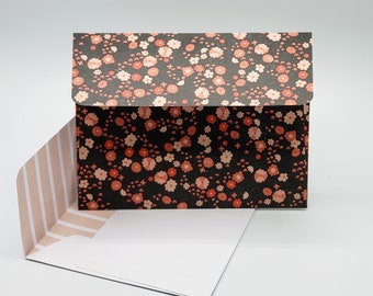 May include: A black envelope with a pink floral pattern. The envelope is lined with pink and white stripes.