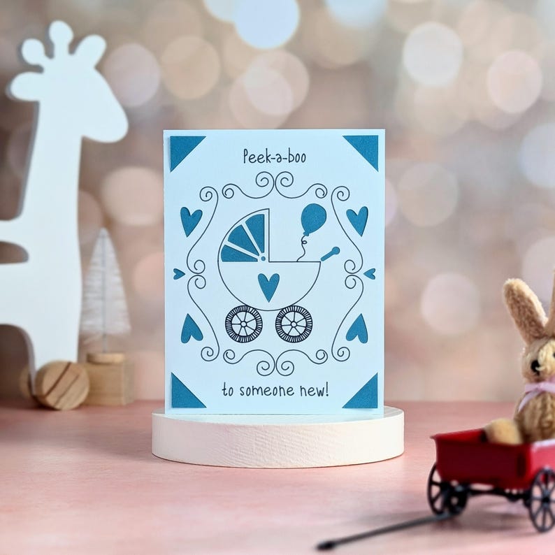 May include: A blue and white card with a baby carriage and a balloon. The card says "Peek-a-boo to someone new!"