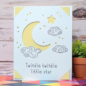 May include: A white card with a yellow crescent moon, a yellow star, and two gray clouds. The card has the text "Twinkle twinkle little star" written on it.