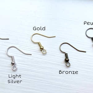 Op de afbeelding: Een assortiment oorhaakjes in verschillende metallic afwerkingen: zilver, licht zilver, goud, brons en tin. Elke haak wordt afzonderlijk weergegeven, met de kleurnaam erboven. De haken zijn ontworpen voor het maken van sieraden.