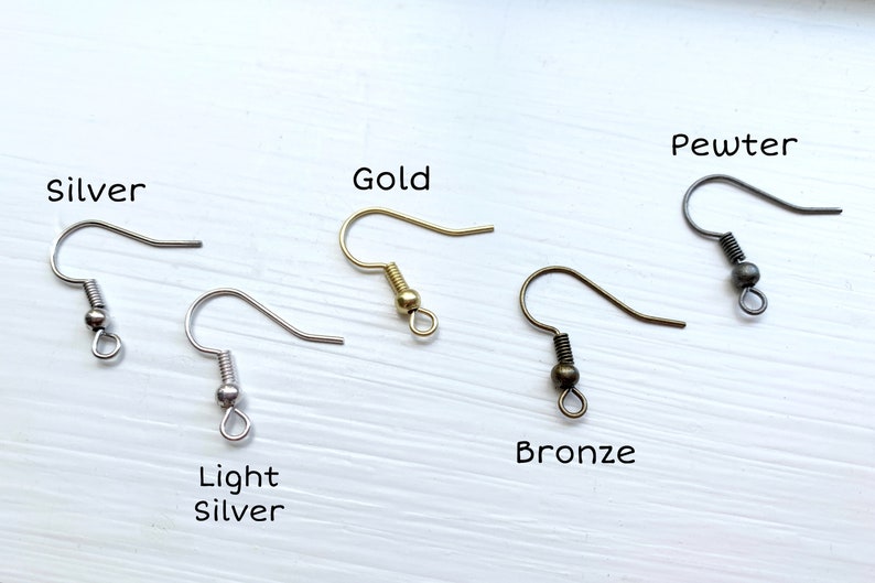 Op de afbeelding: Een assortiment oorhaakjes in verschillende metallic afwerkingen: zilver, licht zilver, goud, brons en tin. Elke haak wordt afzonderlijk weergegeven, met de kleurnaam erboven. De haken zijn ontworpen voor het maken van sieraden.