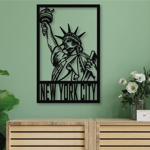 Pode incluir: Arte de parede de metal preto com uma silhueta da Estátua da Liberdade com o texto "NEW YORK CITY" abaixo. A arte está pendurada em uma parede verde acima de um armário de madeira.