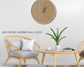 May include: A mid-century modern wall clock with a woven cane design. The clock is hanging on a white wall, and there are two wicker chairs and a coffee table in the foreground.
