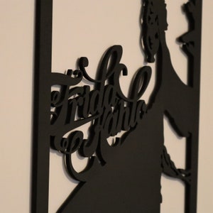 May include: Black silhouette wall art featuring Frida Kahlo with her name in a stylized font.