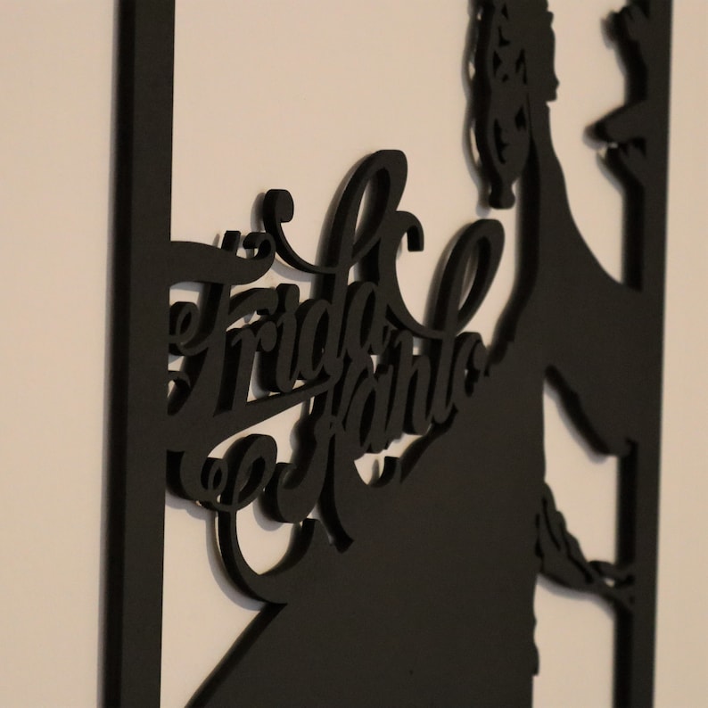 May include: Black silhouette wall art featuring Frida Kahlo with her name in a stylized font.