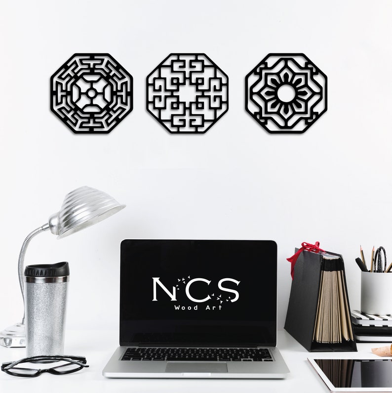 May include: Three black octagonal wall decorations featuring intricate geometric designs. The designs are reminiscent of traditional Asian patterns. The decor is displayed on a white wall with a laptop, lamp, and office supplies in the foreground.