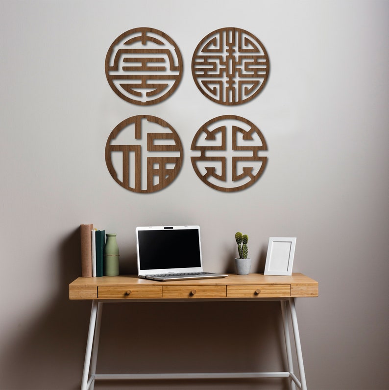 May include: Four brown wooden wall decor pieces in the shape of circles with intricate geometric designs. The decor is hanging on a white wall above a wooden desk with a laptop, a potted plant, and a picture frame.