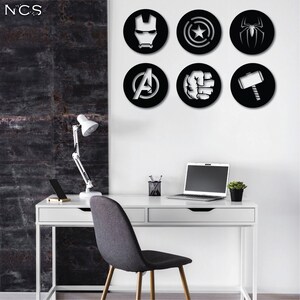 Puede incluir: Seis pegatinas de pared circulares en blanco y negro con logotipos de superh&eacute;roes de Marvel. Los logotipos incluyen Iron Man, Capit&aacute;n Am&eacute;rica, Thor, Hulk, Spider-Man y el logotipo de los Vengadores. Las pegatinas se muestran en una pared blanca sobre un escritorio blanco con una computadora port&aacute;til, una l&aacute;mpara y una silla.