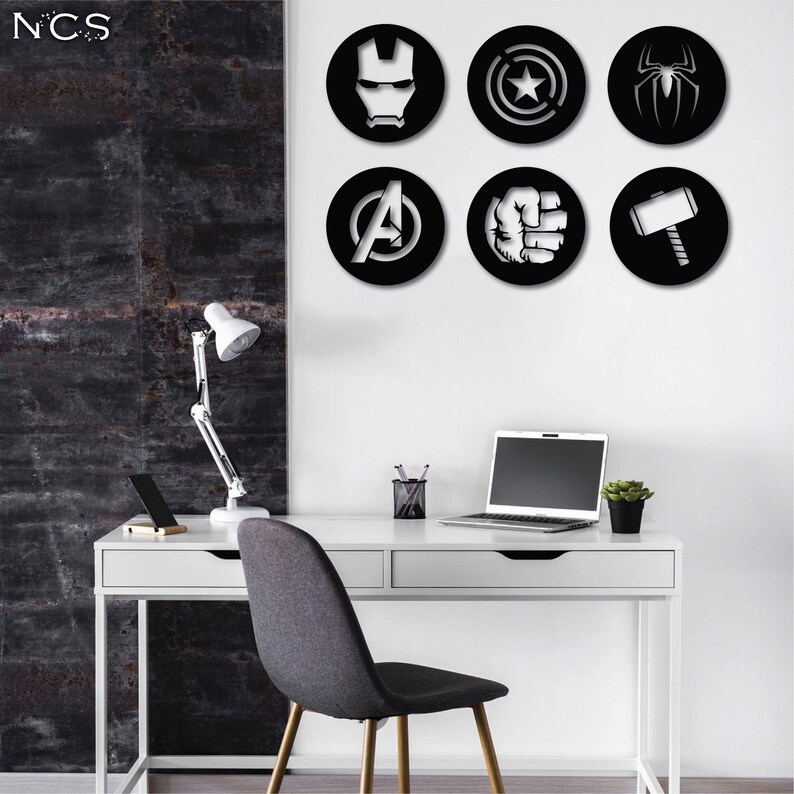 Puede incluir: Seis pegatinas de pared circulares en blanco y negro con logotipos de superh&eacute;roes de Marvel. Los logotipos incluyen Iron Man, Capit&aacute;n Am&eacute;rica, Thor, Hulk, Spider-Man y el logotipo de los Vengadores. Las pegatinas se muestran en una pared blanca sobre un escritorio blanco con una computadora port&aacute;til, una l&aacute;mpara y una silla.