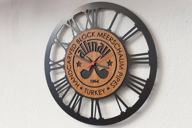May include: Black metal clock with Roman numeral markings and a wooden center featuring the text "Handcarved Block Meerschaum Pipes Altinay 1964 Turkey" and a graphic of two crossed pipes.