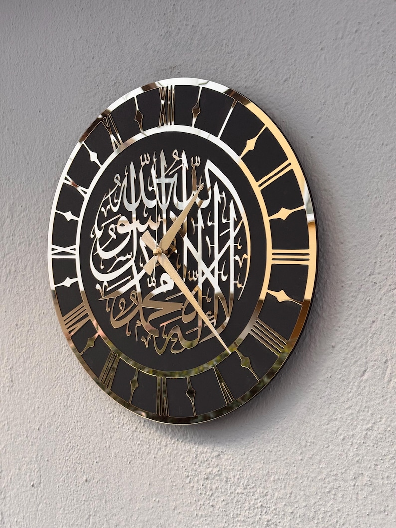 May include: A black and gold clock with Roman numerals and Arabic calligraphy. The clock has a black background and gold accents. The calligraphy is in Arabic and is a religious inscription.