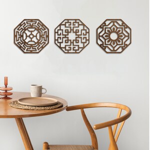 May include: Three wooden wall decorations in the shape of octagons with intricate geometric designs. The designs are in a dark brown colour and are set against a white wall.