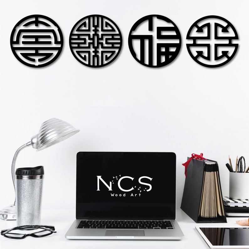 May include: Four black wooden wall decor pieces with intricate geometric designs. The designs are inspired by traditional Chinese symbols. The pieces are arranged in a row on a white wall. The text "NCS Wood Art" is visible on a laptop screen in the foreground.