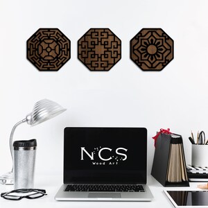 May include: Three wooden wall decorations with geometric designs in black and brown. The designs are octagonal and feature intricate patterns. The pieces are arranged in a row on a white wall.