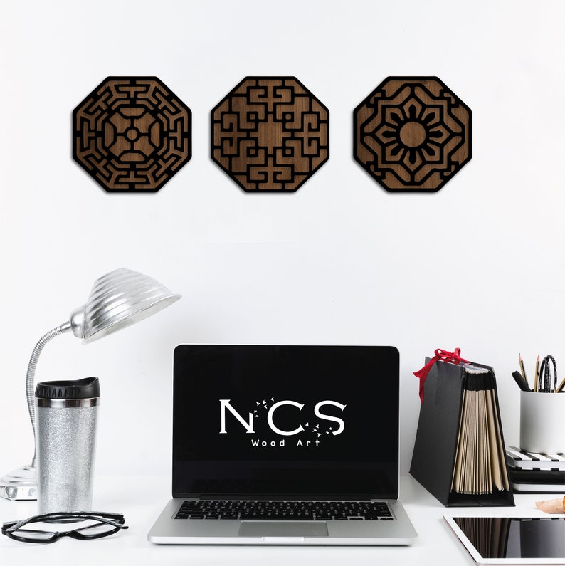 May include: Three wooden wall decorations with geometric designs in black and brown. The designs are octagonal and feature intricate patterns. The pieces are arranged in a row on a white wall.