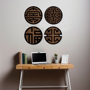 May include: Four round wooden wall decor pieces with black geometric designs. The decor is displayed on a white wall above a wooden desk with a laptop, a potted plant, and a picture frame.