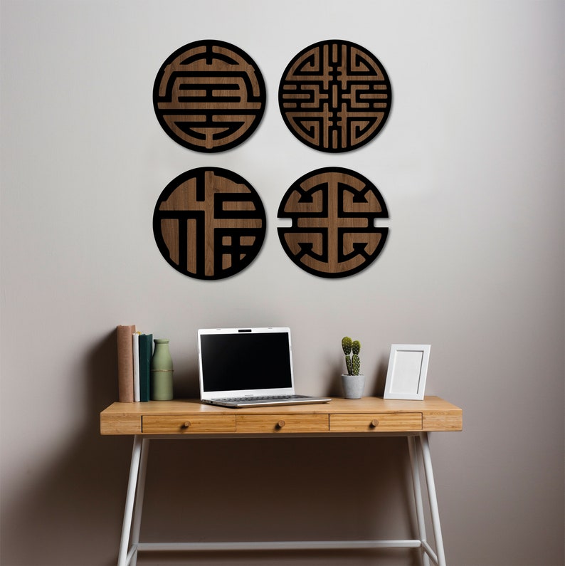May include: Four round wooden wall decor pieces with black geometric designs. The decor is displayed on a white wall above a wooden desk with a laptop, a potted plant, and a picture frame.