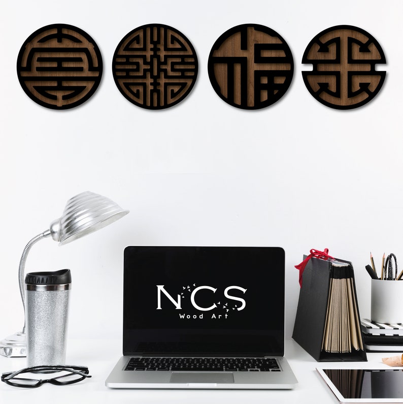 May include: Four round wooden wall decor pieces with intricate geometric designs in black and brown. The designs are similar to Chinese characters. The wall decor is displayed on a white wall with a laptop, a lamp, and office supplies on a white desk in front of the wall.