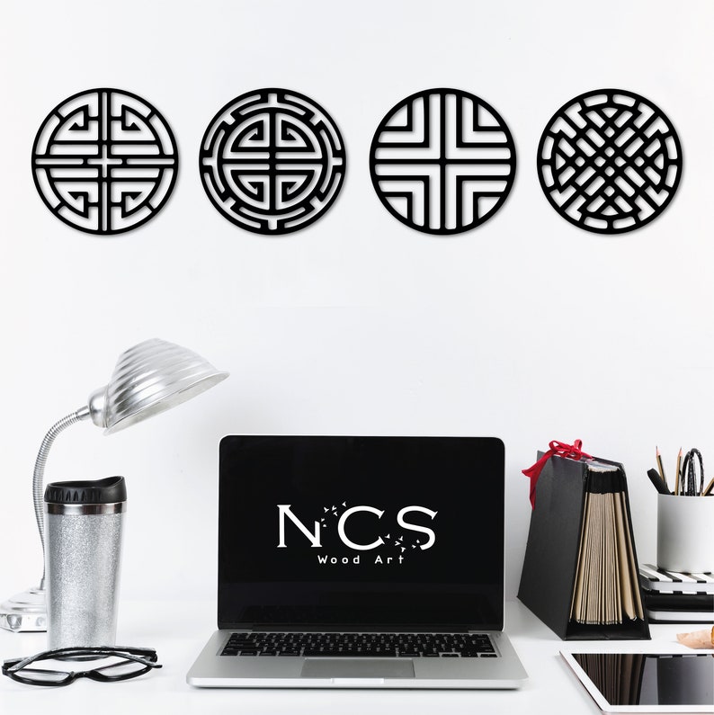 May include: Four black wooden wall decor pieces with geometric designs. The designs are circular and feature intricate patterns. The pieces are arranged in a row on a white wall. The text "NCS Wood Art" is visible on a laptop screen in the foreground.