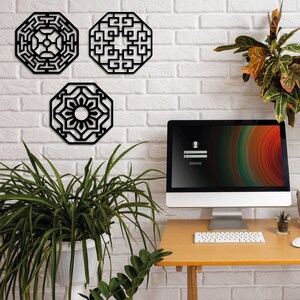 May include: Three black geometric wall decorations in a modern style. The pieces are in the shape of octagons and feature intricate patterns. The decor is displayed on a white brick wall with a potted plant and a computer monitor on a wooden desk below.