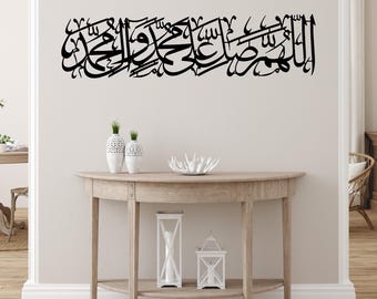 May include: A black calligraphy wall decal with Arabic script, displayed on a white wall above a wooden console table with white decorative objects.