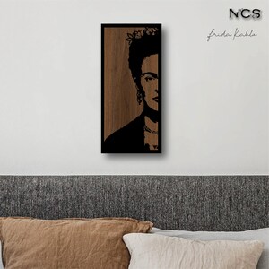 May include: A black and white silhouette of Frida Kahlo's face on a wood background. The image is framed in black.