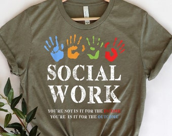 May include: Green t-shirt with a white graphic that says "SOCIAL WORK" with colorful handprints above the text. The text below the handprints says "YOU'RE NOT IN IT FOR THE INCOME YOU'RE IN IT FOR THE OUTCOME"