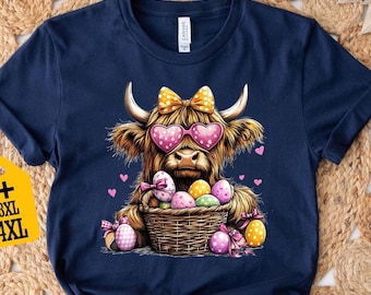 May include: A navy blue t-shirt with a cartoon Highland cow wearing pink heart-shaped sunglasses and a yellow bow. The cow is holding a basket of colorful Easter eggs.