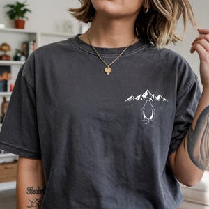A person wearing a gray t-shirt with a graphic design of a penguin and mountains printed on it.