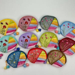 May include: A collection of 11 colorful embroidered coin purses with floral designs. Each purse is made of a different fabric and has a unique pattern. The purses are all in the shape of a half-circle and have a small tassel on the side.