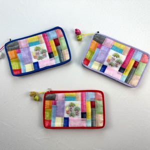 May include: Three rectangular, colorful patchwork pouches with floral embroidery. The pouches have a zipper closure and decorative tassels. The pouches are in blue, purple, and red trim.
