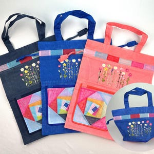 May include: Three tote bags in navy, blue, and coral. Each bag features a colorful geometric pocket, embroidered flowers, and a drawstring closure. The bags have matching handles and decorative trim.