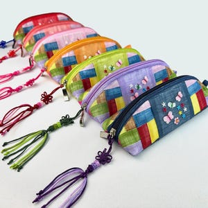 May include: A set of six colorful fabric pencil cases with embroidered butterflies and tassels. The cases are made of patchwork fabric in various colors, including red, orange, yellow, green, blue, and purple.