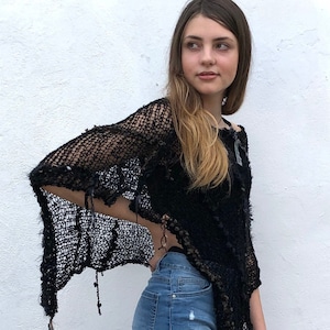 May include: A black crochet poncho with a fringe detail. The poncho is worn over a pair of blue denim shorts.