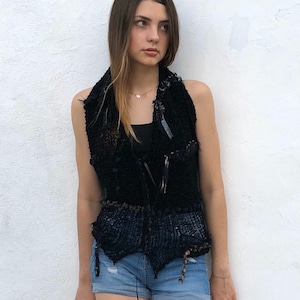 May include: A black sleeveless vest with a crocheted design and a brown belt. The vest has a frayed edge and is made of a textured fabric.