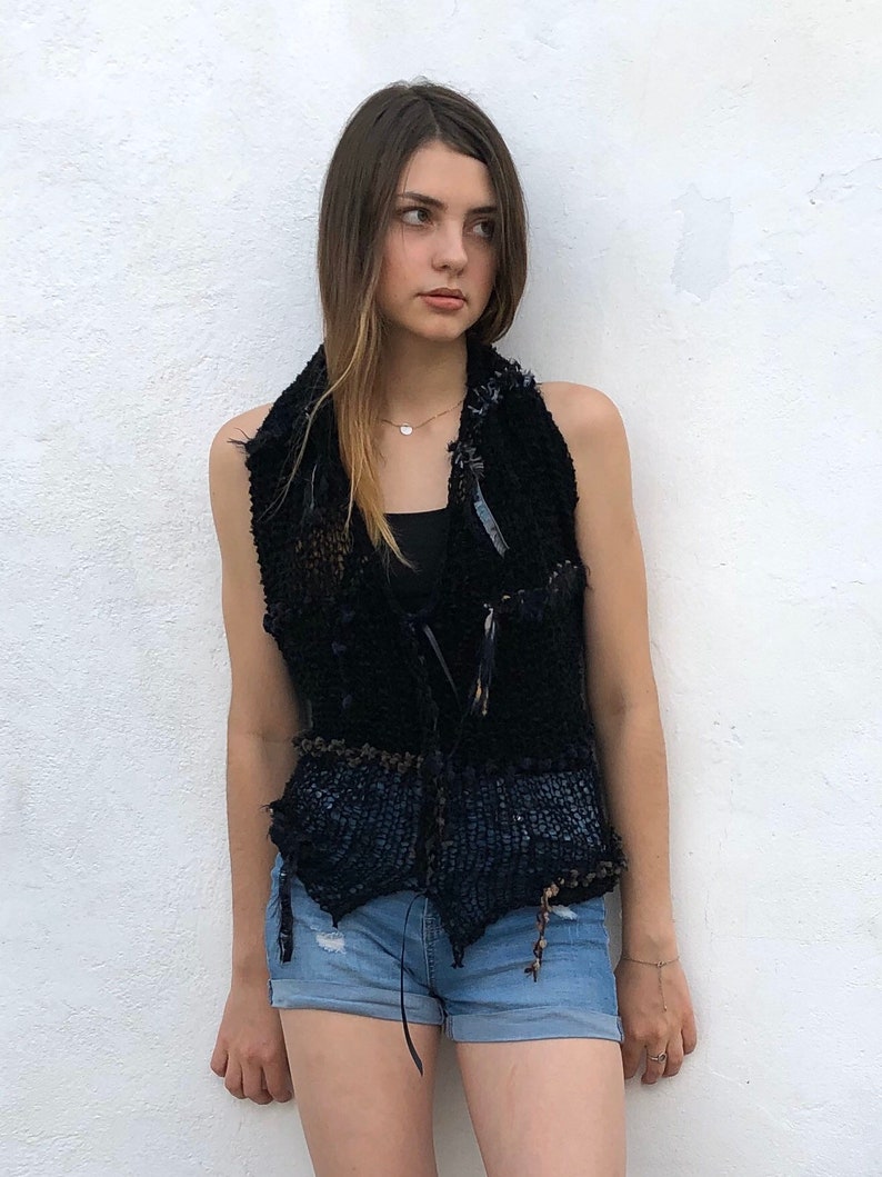 May include: A black sleeveless vest with a crocheted design and a brown belt. The vest has a frayed edge and is made of a textured fabric.