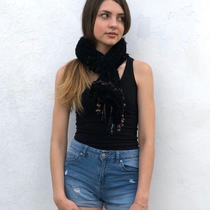 May include: A black fuzzy scarf with brown accents worn around the neck of a person wearing a black tank top and blue denim shorts.