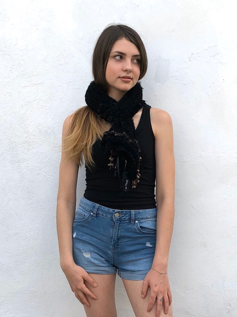 May include: A black fuzzy scarf with brown accents worn around the neck of a person wearing a black tank top and blue denim shorts.