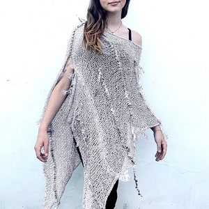 May include: A light gray knitted poncho with a distressed, frayed look. The poncho is asymmetrical and has a loose, flowing fit.