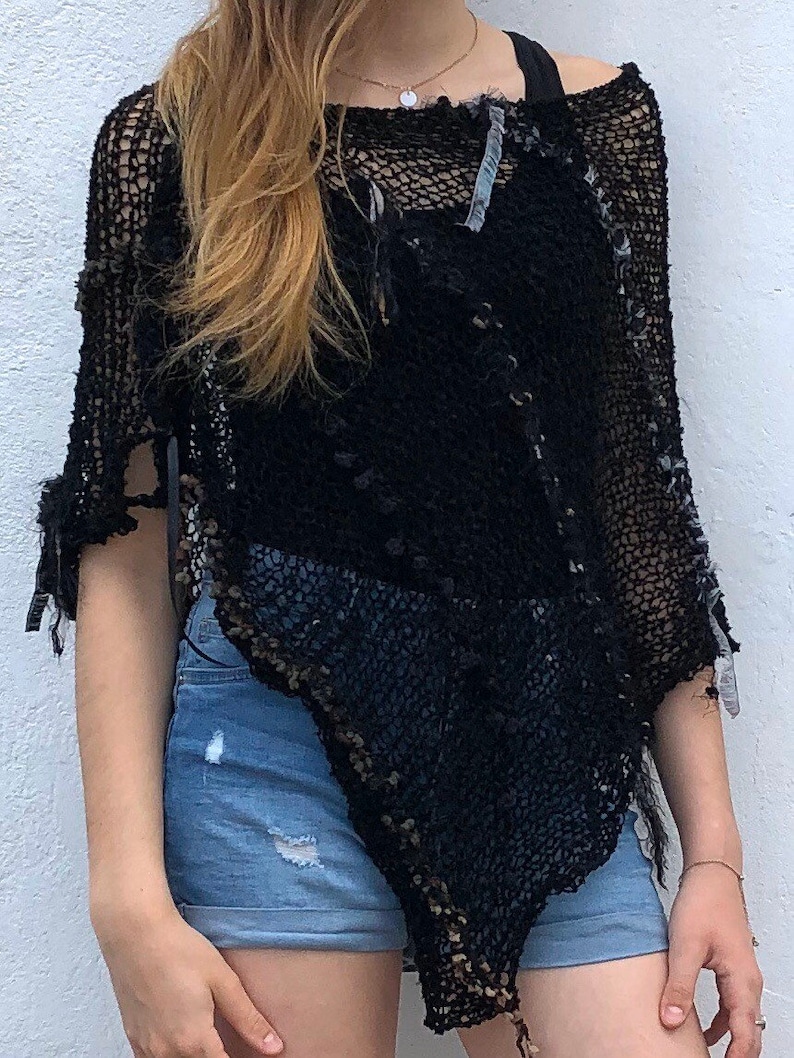 May include: Black crochet poncho with a distressed and open-weave design. The poncho is worn over a black tank top and blue denim shorts.