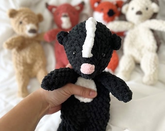 May include: Crochet pattern for a black and white skunk amigurumi toy. The toy has a white stripe down its back and a pink nose.