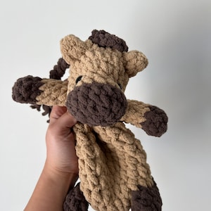 May include: A brown and tan crocheted horse stuffed animal with a brown mane and tail. The horse is held in a hand.