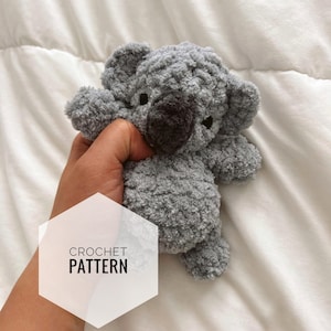 May include: A gray crochet koala bear with a dark brown nose and small black eyes. The koala is made of a soft, textured yarn. The image includes the text "CROCHET PATTERN".