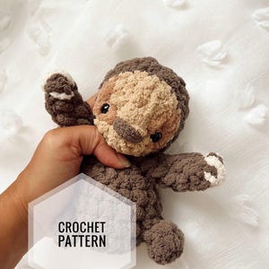 Puede incluir: Un juguete de amigurumi de crochet en forma de perezoso, de color marrón y beige con detalles blancos. El juguete está siendo sostenido en una mano y el texto "CROCHET PATTERN" es visible en la imagen.