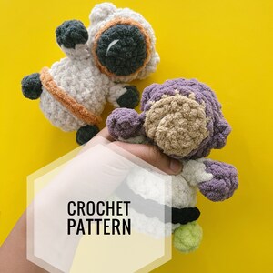 May include: Two crocheted plush toys, one white with a black face and orange trim, and one purple with a brown face, on a yellow background. The text "CROCHET PATTERN" is visible in the image.