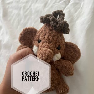 Może przedstawiać: Wzór na szydełku na brązowego pluszowego słonia z brązowym supełkiem na górze. Wzór jest napisany "CROCHET PATTERN" na białym sześciokącie.