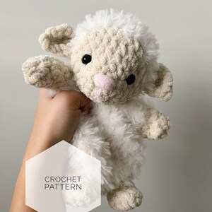 May include: Crochet pattern for a white fluffy lamb amigurumi toy. The lamb has black eyes, a pink nose, and a white fluffy head.