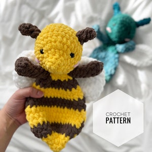 May include: Crochet pattern for a cute bee amigurumi toy. The bee is yellow and brown with white wings. The bee has black eyes and a pink nose.