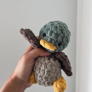 May include: A crocheted plush toy duck with a green head, brown body, and yellow beak and feet.